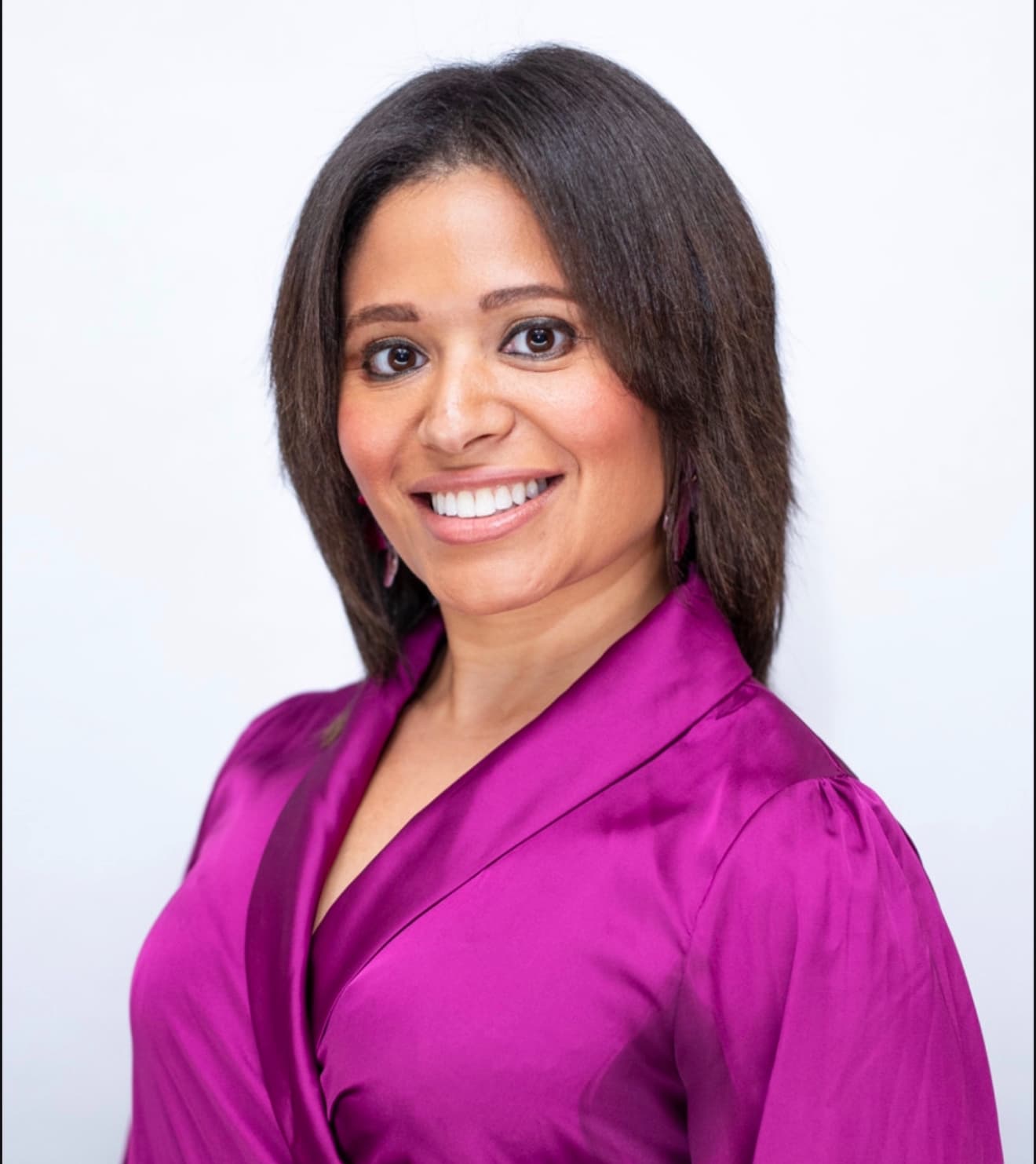 A smiling woman with dark brown hair wearing a vibrant purple satin wrap-style blouse.